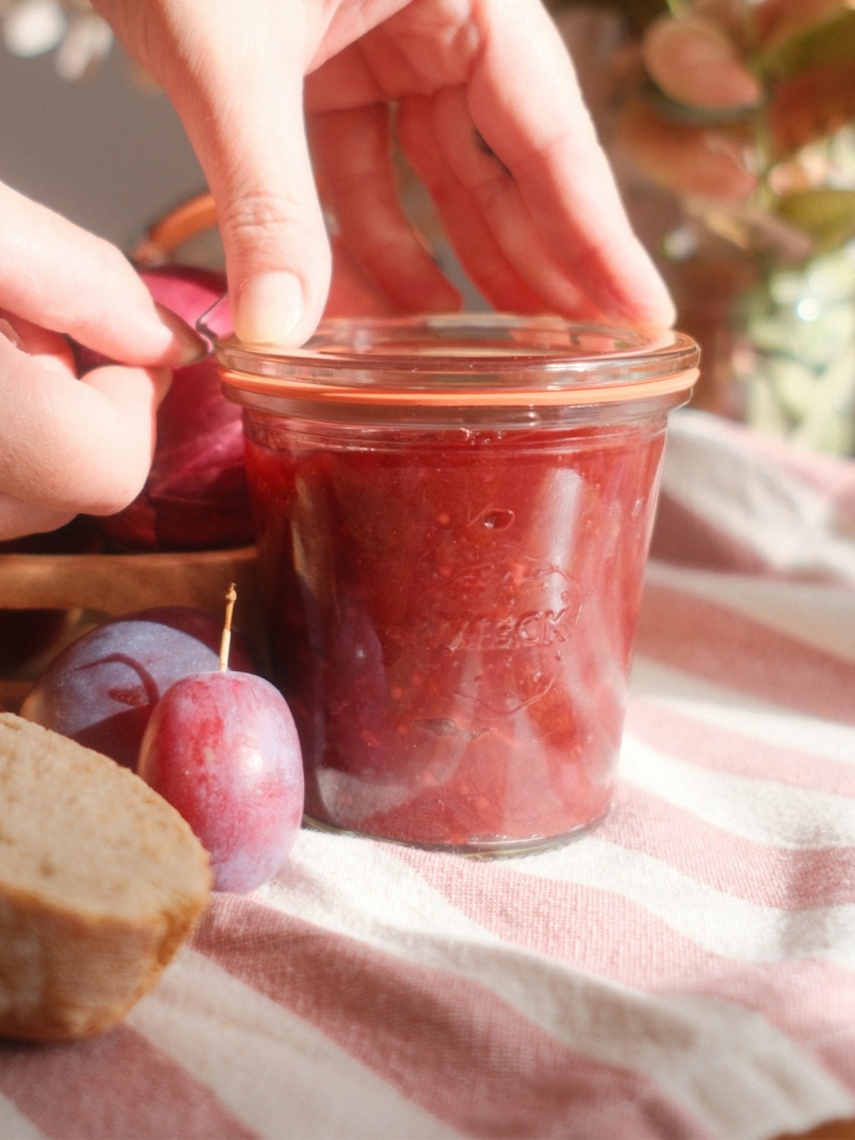 Pots de chutney de prunes disposés avec des prunes, du gingembre et un oignon rouge, recette Deliciously Home.