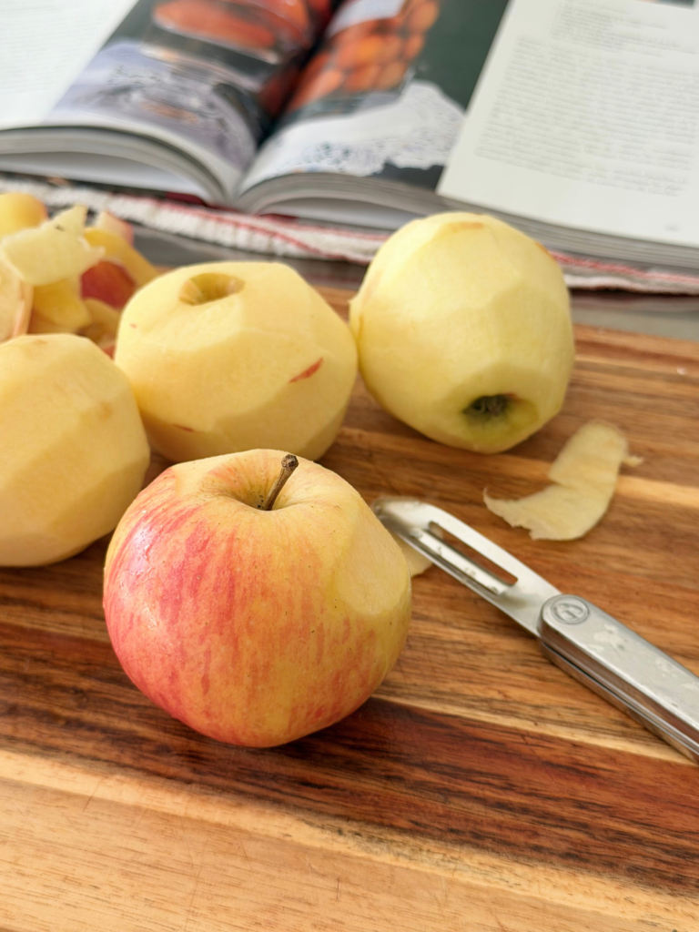 Pommes épluchées sur une planche en bois pendant la préparation du chutney de prunes Deliciously Home.
