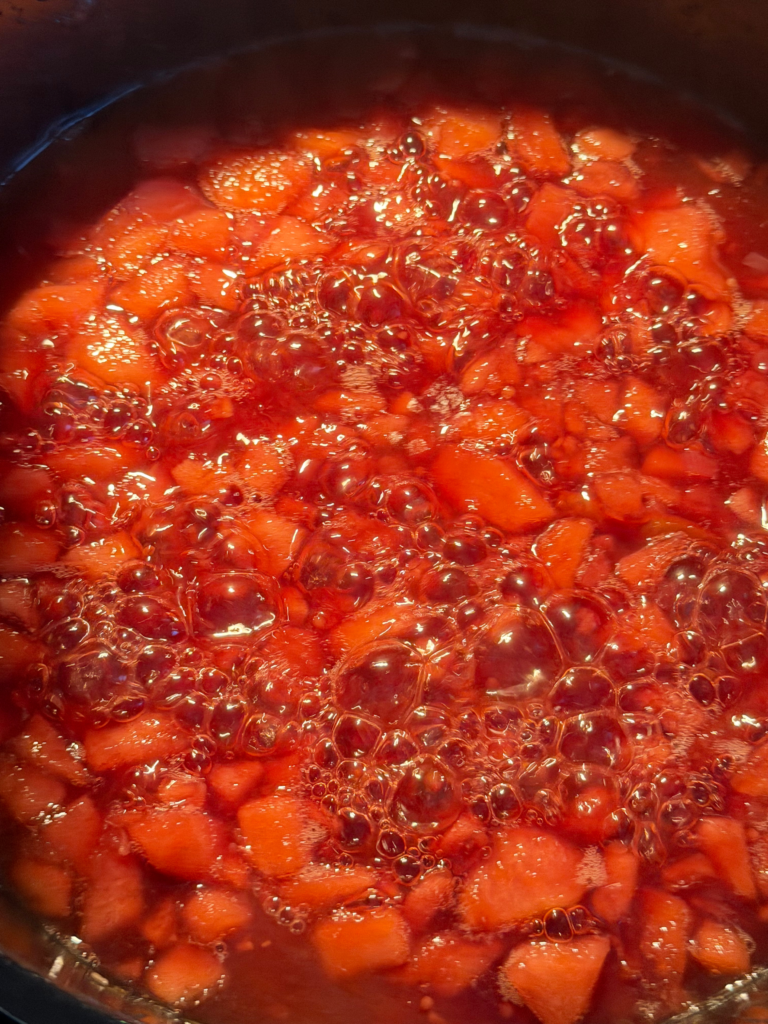 Chutney de prunes en pleine cuisson, avec morceaux de fruits dans un mélange rouge bouillonnant, recette Deliciously Home.
