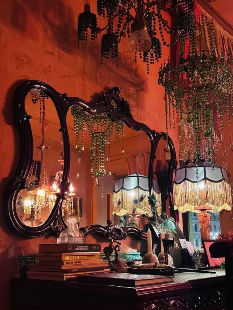 Intérieur whimsigoth aux murs orangés, grand miroir ancien, lustres de perles et lampes à franges dans une lumière tamisée, parmi nos inspirations déco sur Deliciously Home.