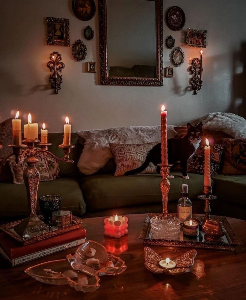 Salon whimsigoth éclairé aux chandelles, avec canapé vert, miroirs anciens, cadres dépareillés et objets accumulés sur une table en bois, parmi nos inspirations déco sur Deliciously Home.