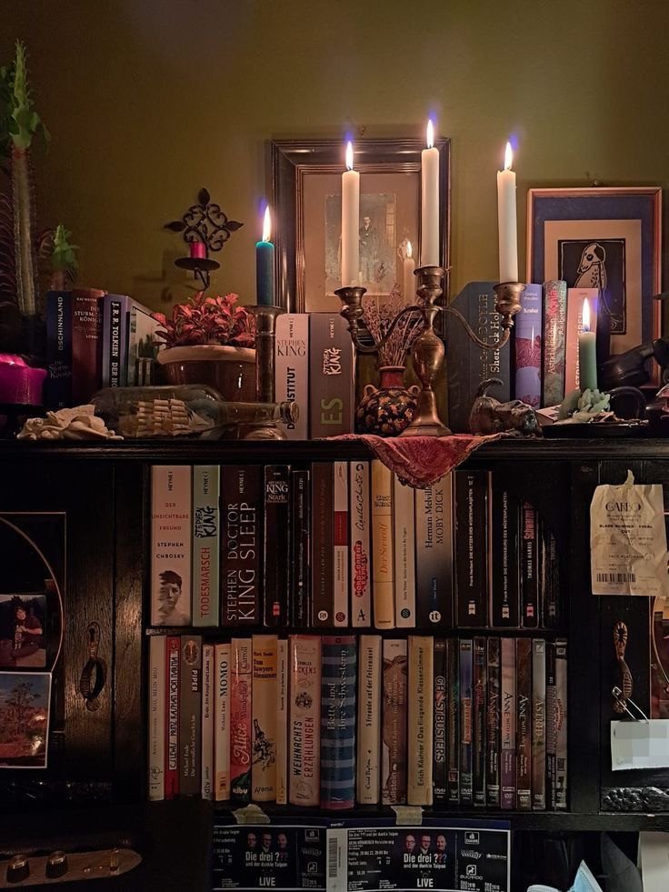 Bibliothèque en bois sombre couverte de livres, chandeliers anciens, bougies colorées, plantes et petits objets personnels, parmi nos inspirations whimsigoth sur Deliciously Home.
