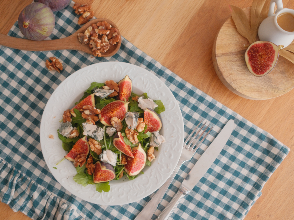 Salade de figues violettes, fromage bleu et noix dressée dans une assiette, avec figues fraîches et vinaigrette à côté. Retrouvez la recette sur Deliciously Home.