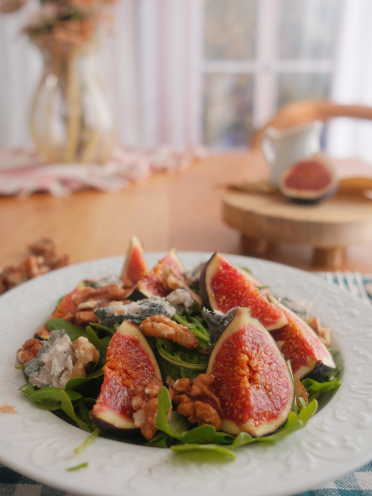 Salade de figues violettes, fromage bleu, cresson et noix, avec les figues fraîches au premier plan. Retrouvez la recette sur Deliciously Home.