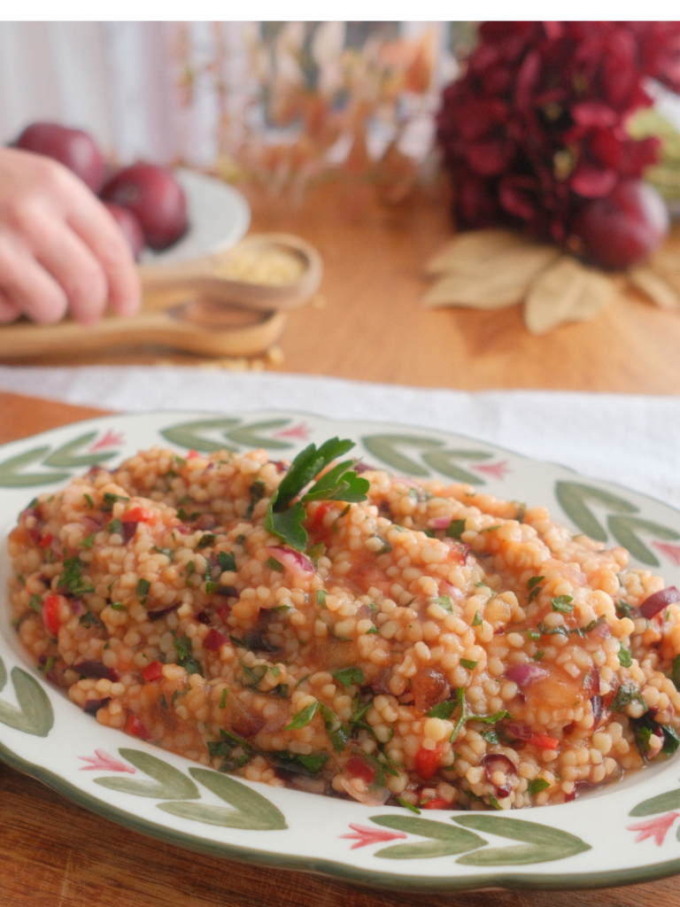 Taboulé aux prunes violettes, couscous à gros grains, herbes fraîches, oignon rouge et piment, servi dans un plat fleuri. Retrouvez la recette sur Deliciously Home.