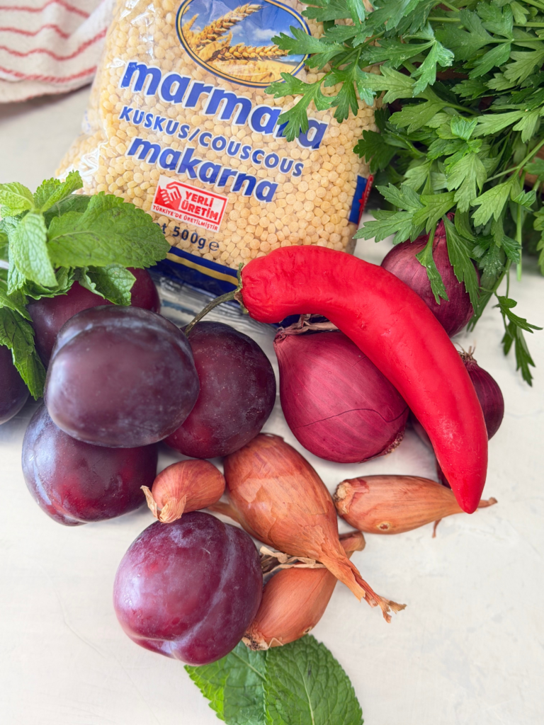 Prunes violettes, couscous à gros grains, menthe, persil, oignons rouges, échalotes et piment rouge réunis pour préparer un taboulé de fin d’été. Retrouvez la recette sur Deliciously Home.