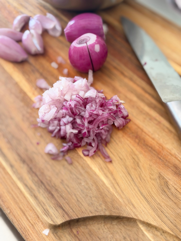 Oignon rouge finement émincé sur une planche en bois, prêt à rejoindre les prunes et les herbes fraîches du taboulé. Retrouvez la recette sur Deliciously Home.