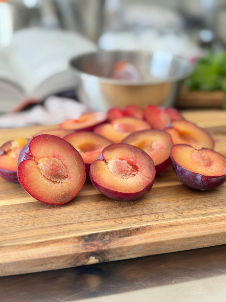 Prunes violettes coupées en deux, dévoilant leur chair jaune orangé avant d’être détaillées pour le taboulé de fin d’été. Retrouvez la recette sur Deliciously Home.